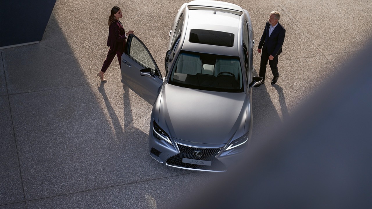 A woman and man walking towards a parked Lexus LS