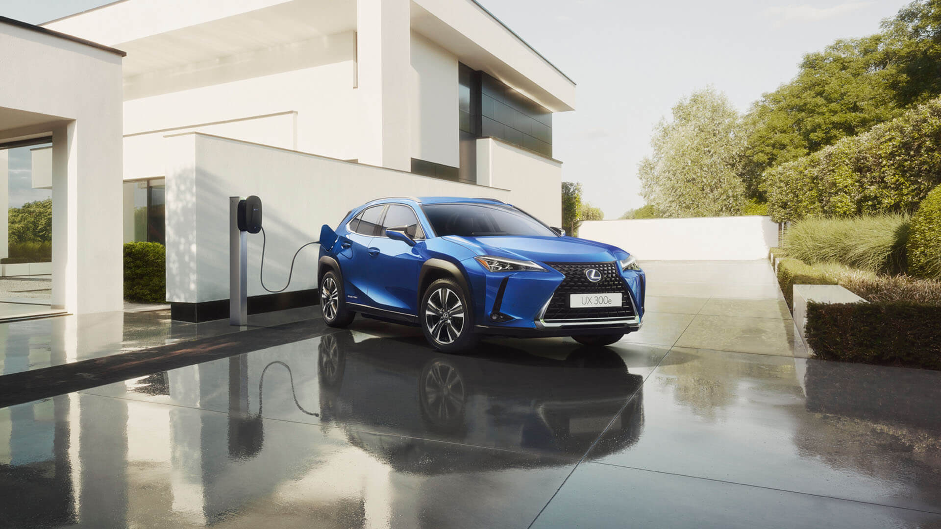 A Lexus UX 300e parked outside a house plugged into a charging station